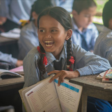A girl from a village in the mountains of Nepal is attending school and laughing in the classroom.