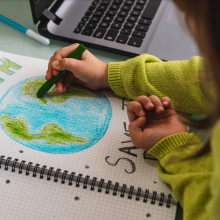 A little girl draws the earth with wax colors on school notebook for Earth Day.