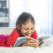 Una niña está leyendo un libro y sonriendo.