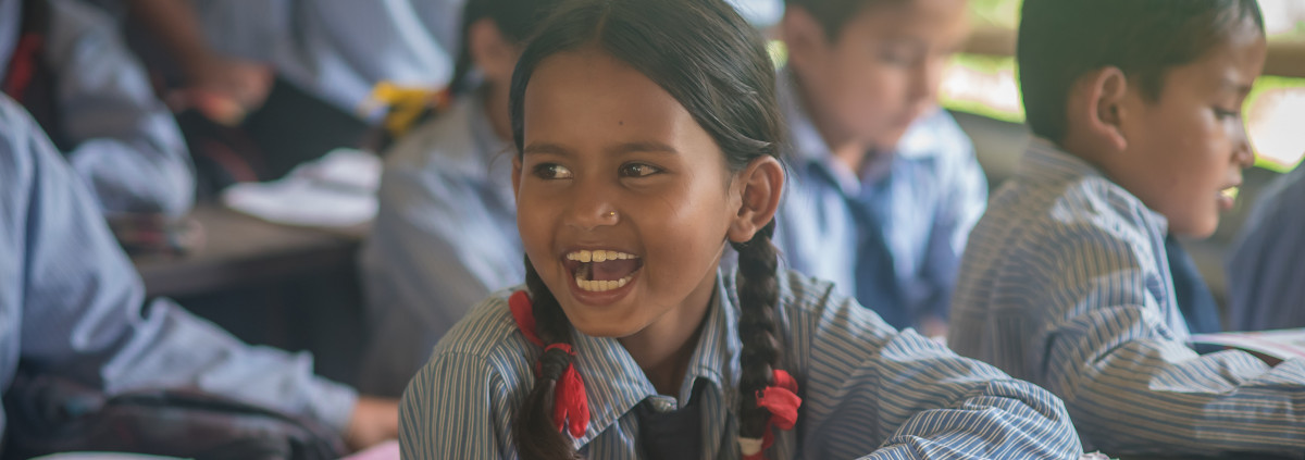 A girl from a village in the mountains of Nepal is attending school and laughing in the classroom.